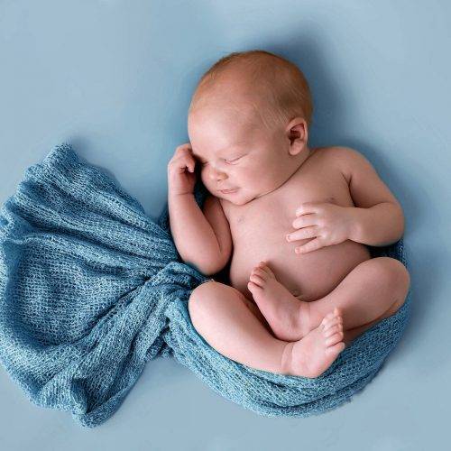 Authentische Neugeborenenfotografie - Junge in blaues Tuch gehüllt - fotografiert von Siebenschön Photography in Beckum
